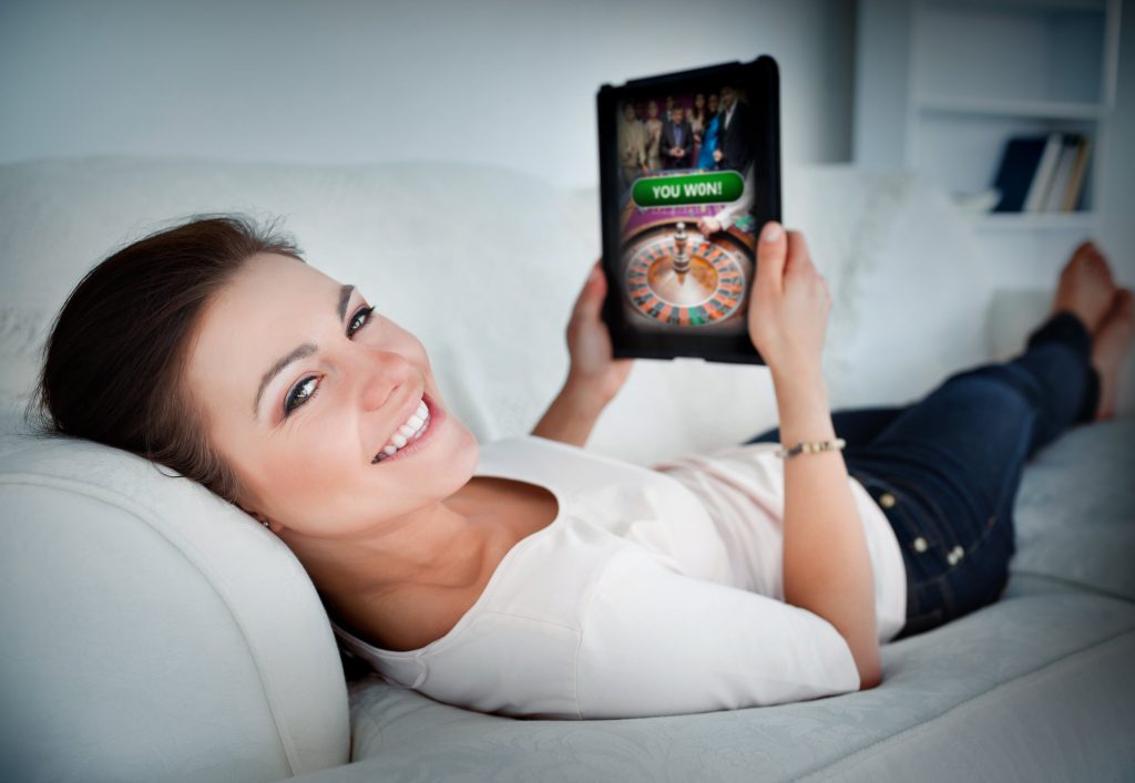 Wanita bermain di kasino online di tablet di rumah, berbaring di sofa